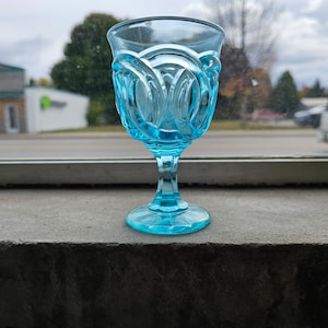 Peut inclure: Un gobelet en verre bleu clair avec un motif décoratif. Le gobelet a un bol rond et une tige haute.