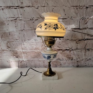 Op de afbeelding: Een witte en blauwe bloemenlamp met een witte kap. De lamp heeft een gouden voet en een witte marmeren voet.