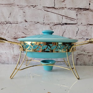 May include: A vintage turquoise chafing dish with a gold-toned metal stand and a decorative cut-out design. The dish has a lid and a small, round base.