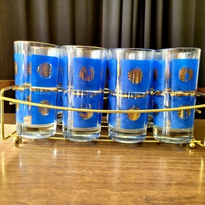 May include: Set of six blue and gold highball glasses in a gold metal rack with wooden handles. The glasses have a gold rim and a blue design with gold accents.