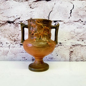 Peut inclure: Un vase en céramique brun et vert avec un motif floral et deux anses. Le vase a une surface texturée et une base arrondie.