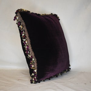 May include: A deep purple velvet pillow with a decorative gold and purple tassel trim.
