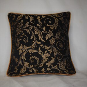 May include: Square cushion with a black backdrop and a gold floral design. The cushion has gold edging. The pattern features swirling leaves and floral motifs. Suitable for home decor, this cushion measures approximately 40cm x 40cm.