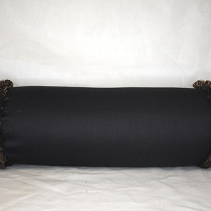 May include: Black cylindrical pillow with gold fringe trim.