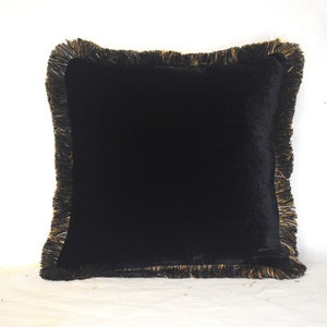 May include: Black velvet cushion with gold fringe trim. The cushion is square shaped and has a soft, luxurious feel.