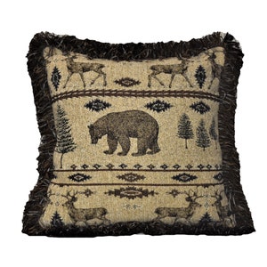 Puede incluir: Cojín decorativo cuadrado con un diseño temático de la naturaleza. Presenta un oso pardo, ciervos y árboles sobre un fondo beige. Los bordes están adornados con una franja marrón oscuro. El cojín tiene una estética rústica de estilo cabaña.