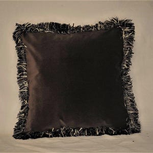 Cojín decorativo de terciopelo marrón oscuro con flecos dorados en marrón topo para sofá o cama.