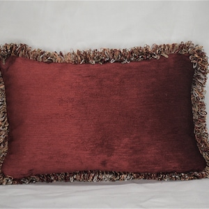 May include: A burgundy pillow with a fringed border. The fringe is a mix of brown, beige, and white.