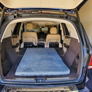 May include: The back of a blue SUV with the tailgate open, revealing a blue mattress in the cargo area. The SUV has a chrome bumper and a black interior.