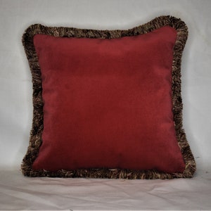 May include: A red throw pillow with a brown fringe border.