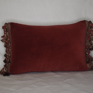 May include: A burgundy pillow with a brown and gold tassel trim.