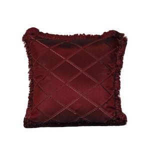 May include: A burgundy throw pillow with a diamond pattern and a fringed border.