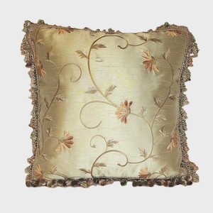 Puede incluir: Un cojín decorativo cuadrado con un fondo verde claro y un diseño floral bordado. El cojín presenta un patrón detallado de flores y vides en tonos marrones y beige. Los bordes están adornados con una franja decorativa.