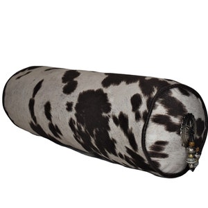 May include: A cylindrical pillow covered in a black and white cowhide pattern with a silver concho and beaded accents.