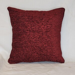 May include: A deep red square throw pillow with a textured fabric.