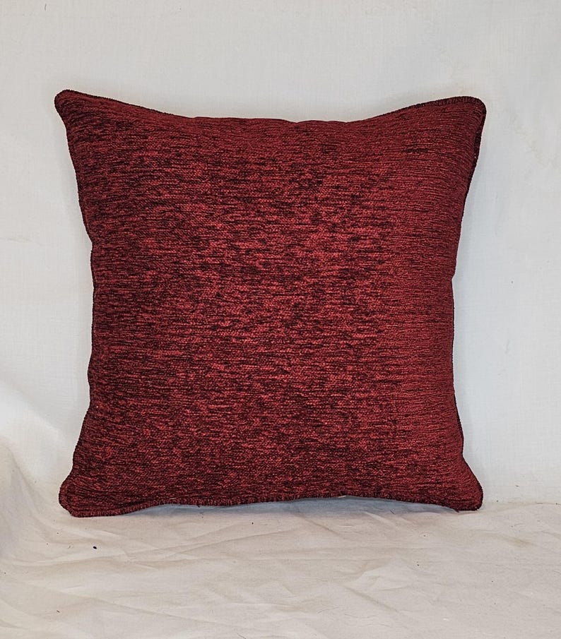May include: A deep red square throw pillow with a textured fabric.