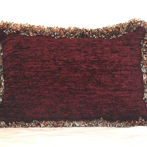 Könnte beinhalten: Ein rechteckiges Kissen in Burgunderrot mit einem Fransenrand in Braun-, Gold- und Silbertönen.