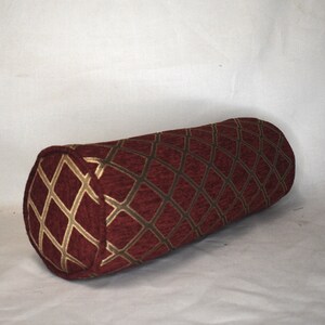 May include: A burgundy and gold cylindrical pillow with a diamond pattern.