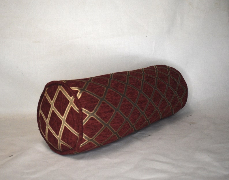 May include: A burgundy and gold cylindrical pillow with a diamond pattern.