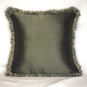 May include: A green pillow with a decorative fringe border. The pillow is made of a soft, silky fabric.