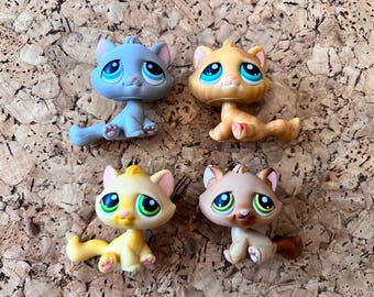 May include: Four cat figurines in shades of blue, yellow, and tan, each with large eyes. The toys are in different poses. These collectible figures are likely part of a larger set.