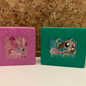 Puede incluir: Dos marcos cuadrados de plástico de Littlest Pet Shop. Uno es rosa con un gráfico de conejo, el otro es verde con un gráfico de perro. Ambos marcos tienen el logotipo de Littlest Pet Shop y detalles florales.