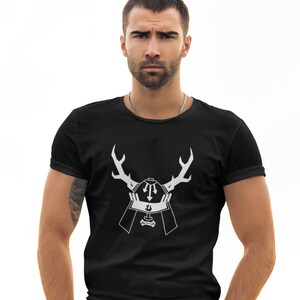 May include: A black t-shirt with a white graphic of a samurai helmet with antlers. The man is wearing black jeans and a black belt. He is standing in front of a motorcycle.