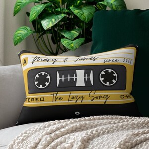May include: A black and yellow throw pillow with a cassette tape design. The text on the cassette tape reads "A Mary & James since 2013, The Lazy Song, C-90, Stereo".