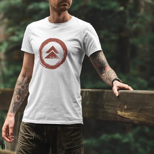 May include: White t-shirt with a red circle and a stylized symbol of two triangles inside. The symbol is reminiscent of a mountain range.