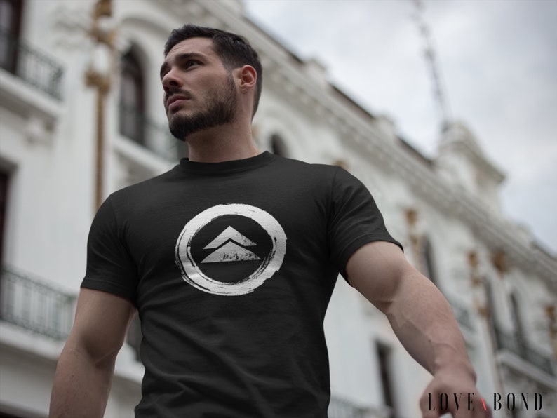 May include: A black t-shirt with a white graphic of a stylized mountain range inside a circle. The graphic has a distressed, hand-painted look.