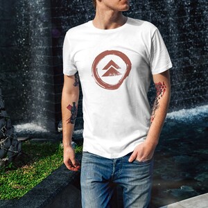 May include: A white t-shirt with a brown circle and a stylized arrow design. The arrow is pointing upwards.