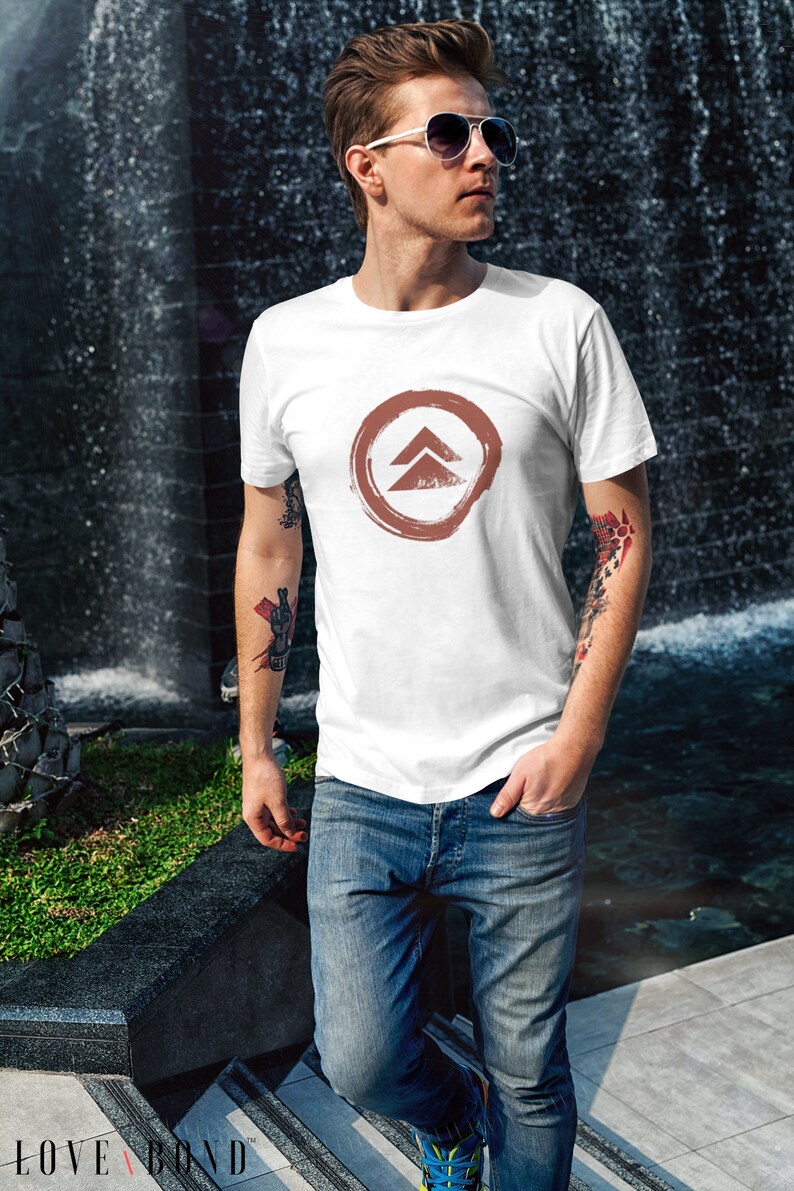 May include: A white t-shirt with a brown circle and a stylized arrow design. The arrow is pointing upwards.