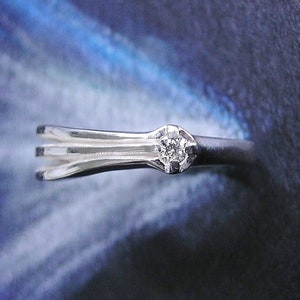 May include: A silver ring with a single, clear diamond set in the center. The ring has a simple, elegant design with three bands.