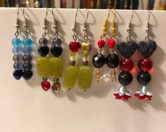 May include: Assortment of handmade earrings featuring various colors and materials, including green jade, red and black beads, and silver heart charms.