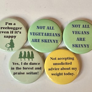 May include: Five round green and yellow buttons with humorous text about vegetarians, vegans, and tree huggers. The text on the buttons reads: "I'm a treehugger even if it's sappy", "NOT ALL VEGETARIANS ARE SKINNY", "NOT ALL VEGANS ARE SKINNY", "Yes, I do dance in the forest and praise seitan!" and "Not accepting unsolicited advice about my weight today."