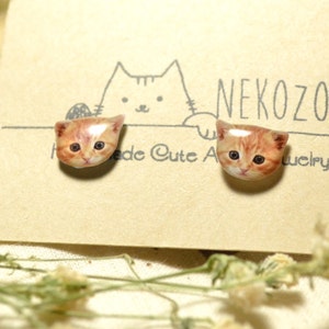 May include: A pair of cat face earrings with a white background. The earrings are made of polymer clay and feature a realistic depiction of a cat's face. The earrings are labelled "NekoZoo Cute Animal Jewellery".