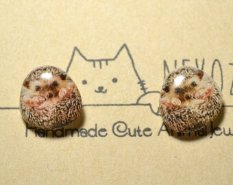 May include: A pair of hedgehog earrings with a brown and white pattern. The earrings are on a brown card with the text "NEVOZOO Handmade Cute Animal Jewelry".