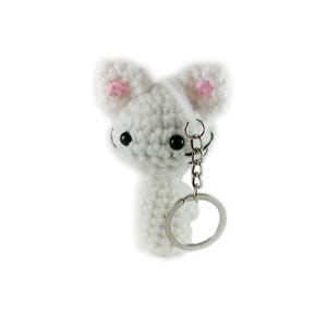 May include: A white crocheted cat keychain with pink inner ears and black eyes. The cat is attached to a silver-colored metal keyring. The keychain is a handmade item.