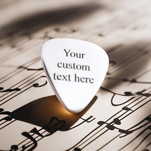 Könnte beinhalten: Ein weißer Gitarrenplektrum mit dem Text "Your custom text here" auf einem Notenblatt.