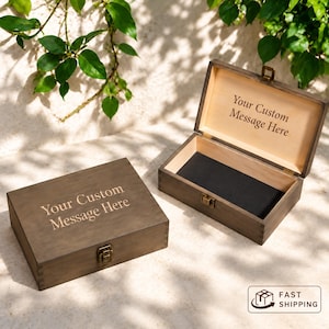 May include: Two rectangular wooden boxes with a dark brown finish and metal latches. One box is closed with the text "Your Custom Message Here" engraved on the lid. The other box is open, revealing a black interior and the same text inside.
