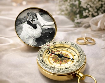 May include: A gold-toned pocket compass with a hinged lid featuring a black and white photograph of a couple in wedding attire. The compass face displays cardinal directions, degree markings, and a central needle with a fleur-de-lis design.