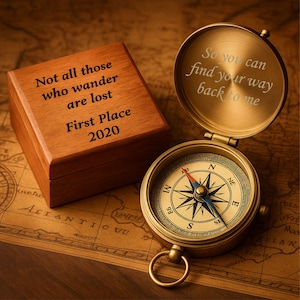 Peut inclure: Une boussole en laiton de style vintage avec un couvercle ouvert, révélant une rose des vents détaillée. Le couvercle est gravé des mots "So you can find your way back to me." À côté, une boîte en bois avec l'inscription "Not all those who wander are lost. First Place 2020."