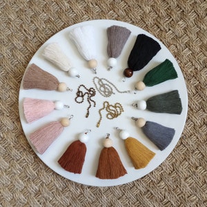 May include: A white plate with 14 different colored tassels with wooden beads and metal chains. The tassels are arranged in a circle on the plate.