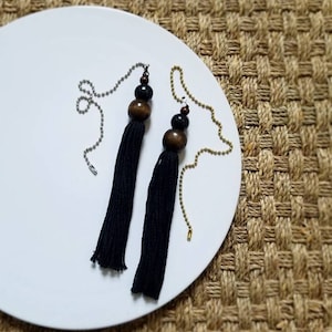 May include: Two black tassel pulls with wooden beads. The beads are brown and black. The tassels are hanging from a silver chain.