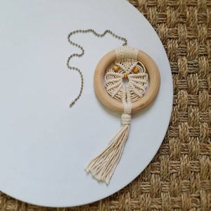 May include: A white macrame owl dreamcatcher with a wooden ring and a tassel hanging from a silver chain.