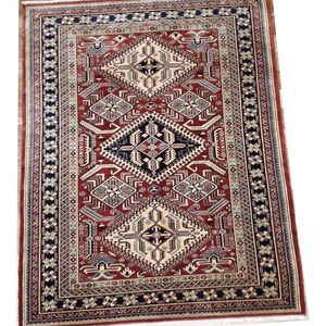 May include: A red, blue, and cream colored rug with a geometric pattern. The rug has a border with a repeating pattern of stars and flowers.
