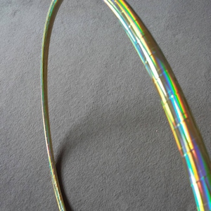 May include: A gold-coloured hoop with iridescent rainbow stripes. The hoop is made of plastic and is flexible.
