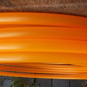May include: A set of orange plastic hoops, stacked on top of each other. The hoops are flexible and appear to be made of a durable material.