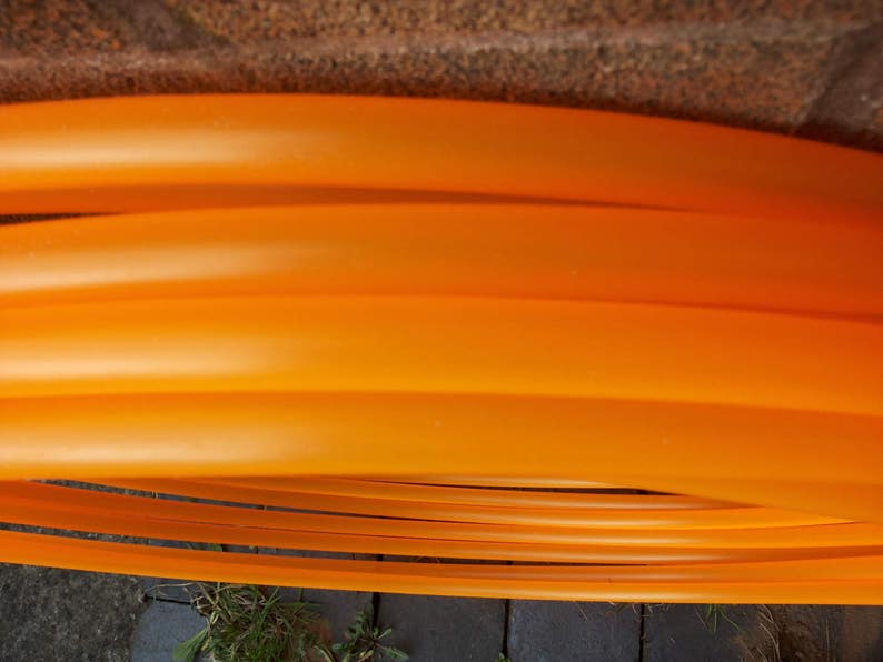 May include: A set of orange plastic hoops, stacked on top of each other. The hoops are flexible and appear to be made of a durable material.