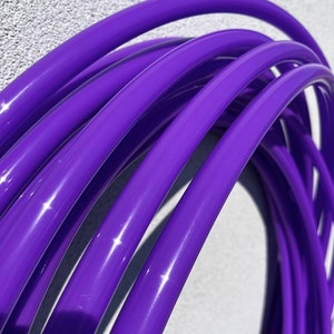 May include: Multiple purple plastic hula hoops stacked together. The hoops are shiny and have a smooth finish.